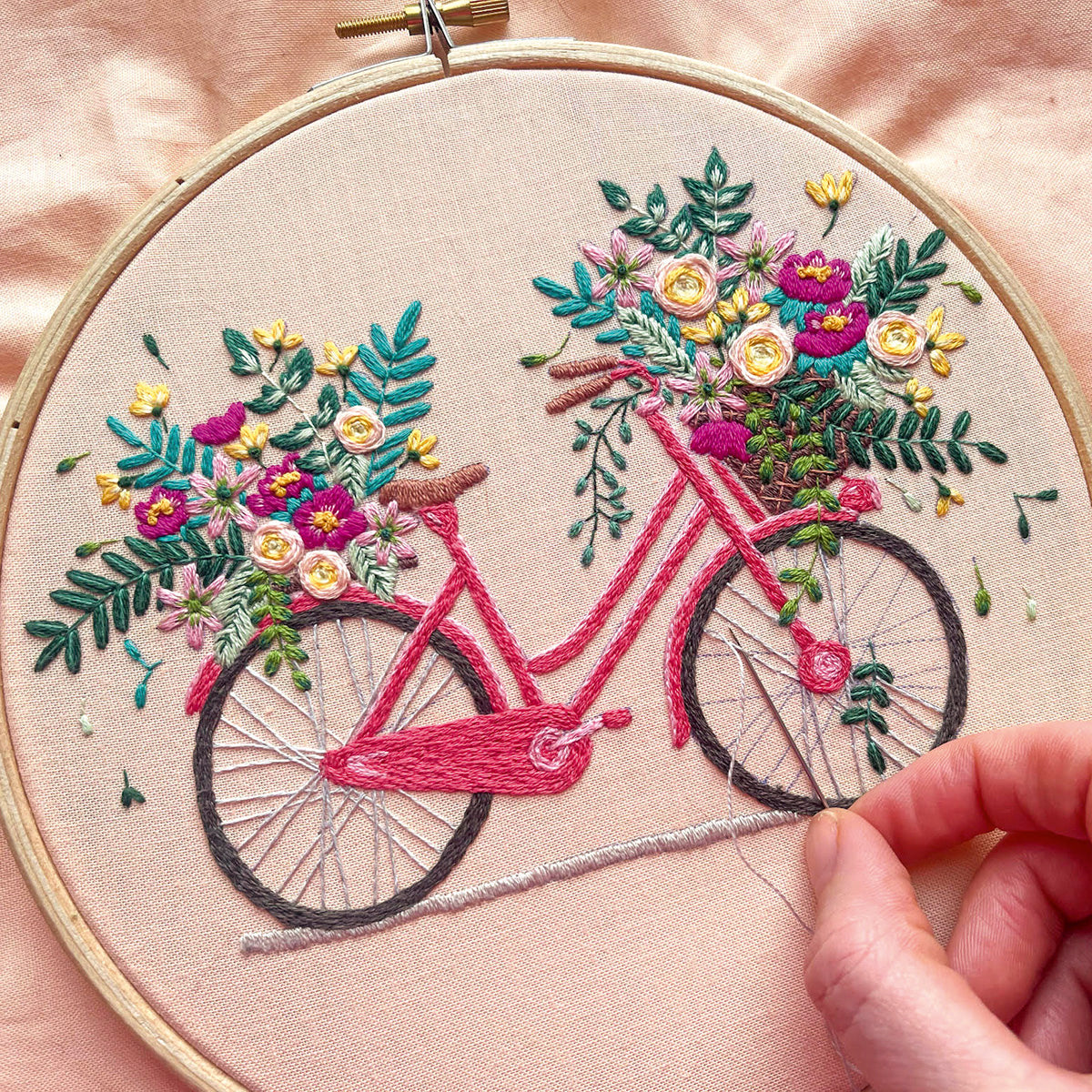 Embroidery hoop with a bicycle and floral design on beige fabric.