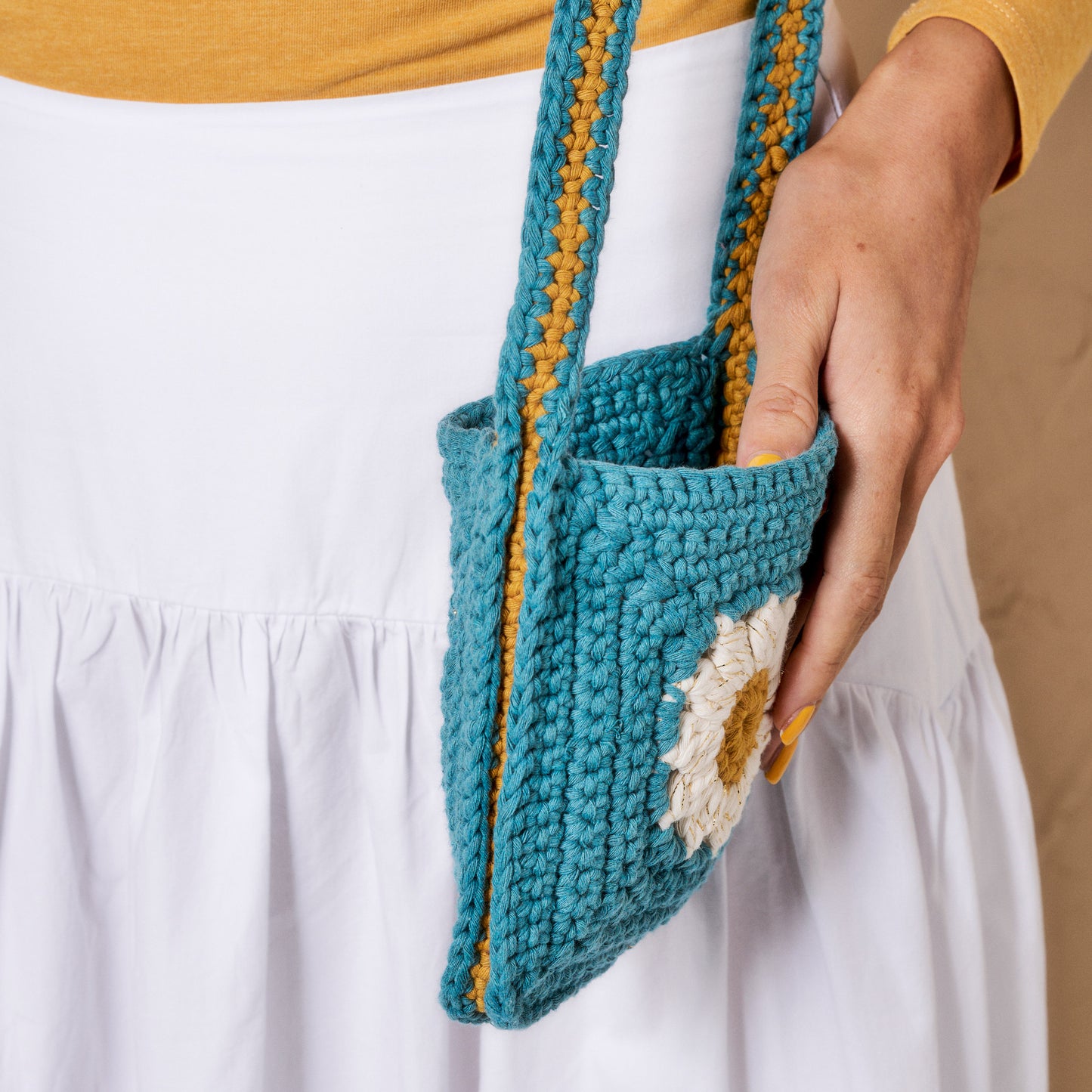 Person holding a teal crochet bag with yellow accents
