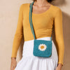 Person wearing a mustard yellow top and white skirt with a blue crochet bag featuring a flower design.