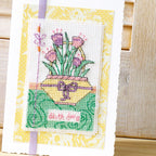 Cross-stitched card with flowers and a bow on a yellow background