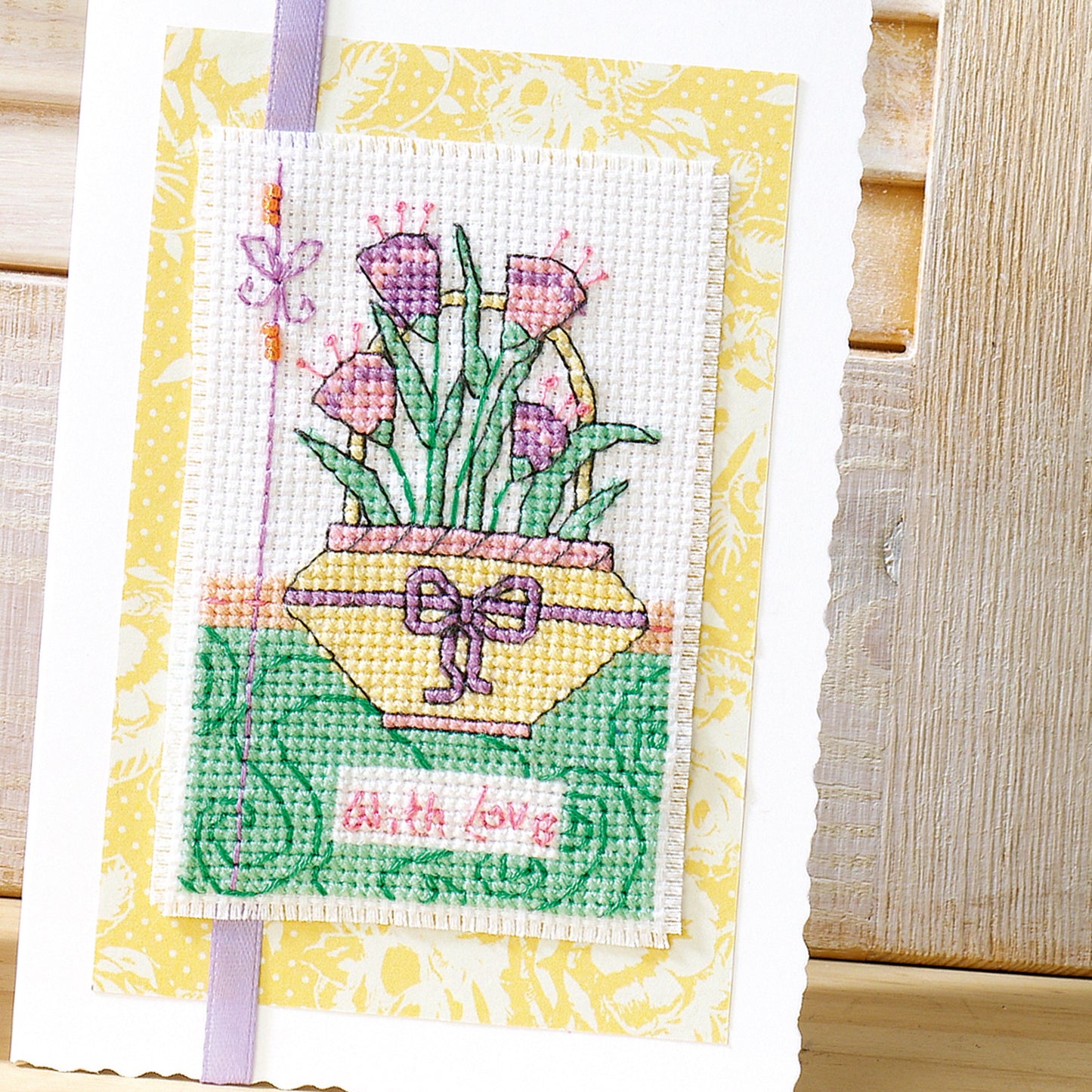 Cross-stitched card with flowers and a bow on a yellow background