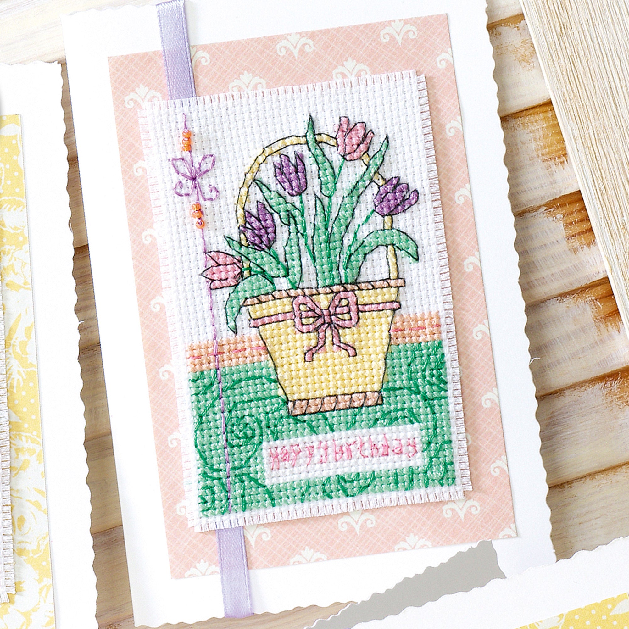 Cross-stitched basket of tulips on a pink card with a ribbon.