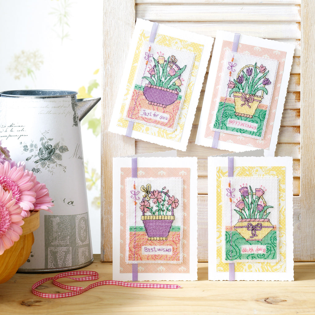 Four cross-stitched cards with floral designs on a wooden surface.
