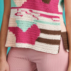 Colorful crocheted heart-patterned bag held by a person against a blue background