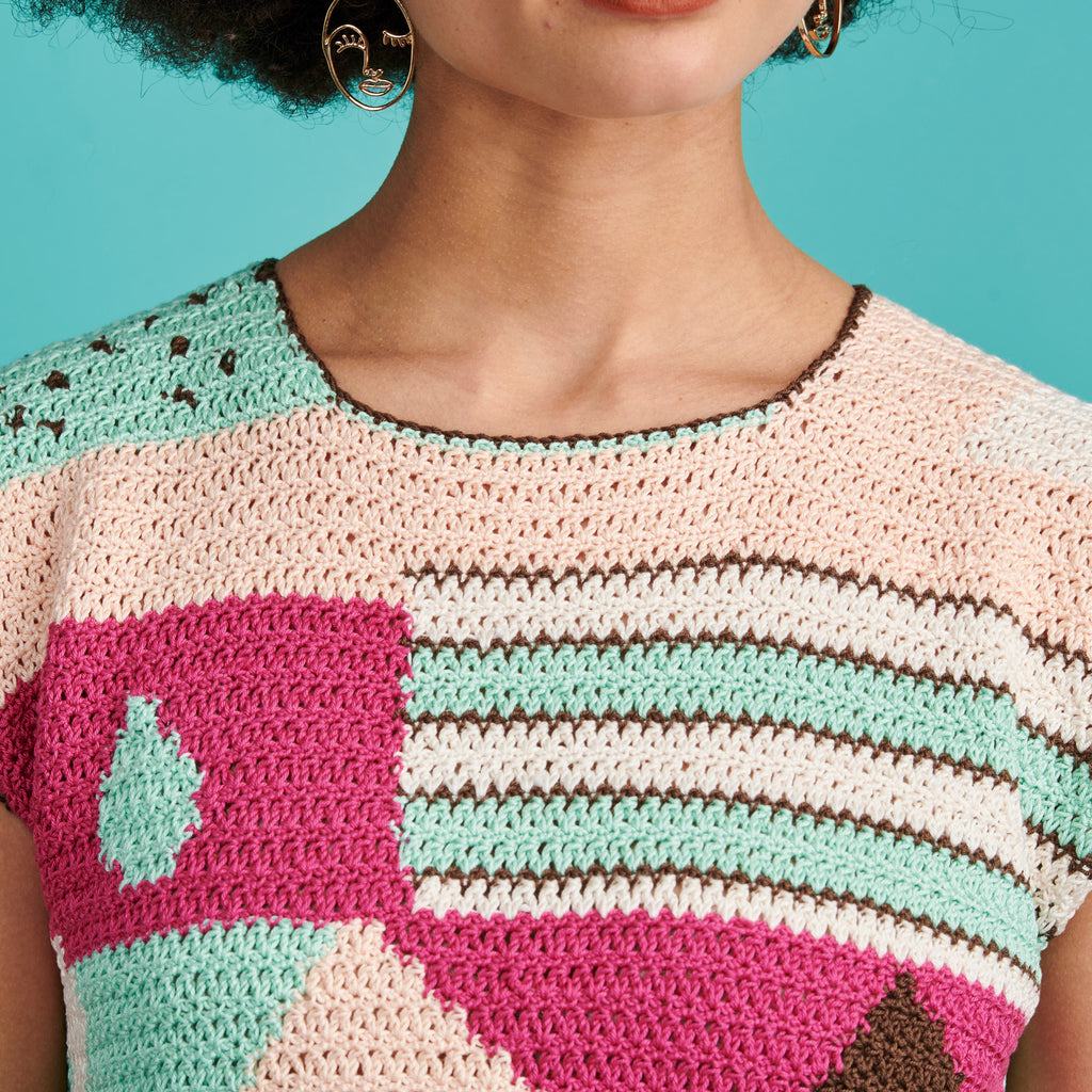 Close-up of a person wearing a colorful crochet top with geometric patterns against a teal background.