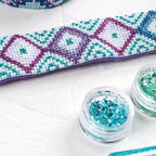 Cross-stitched heart design with two containers of glitter on a white surface