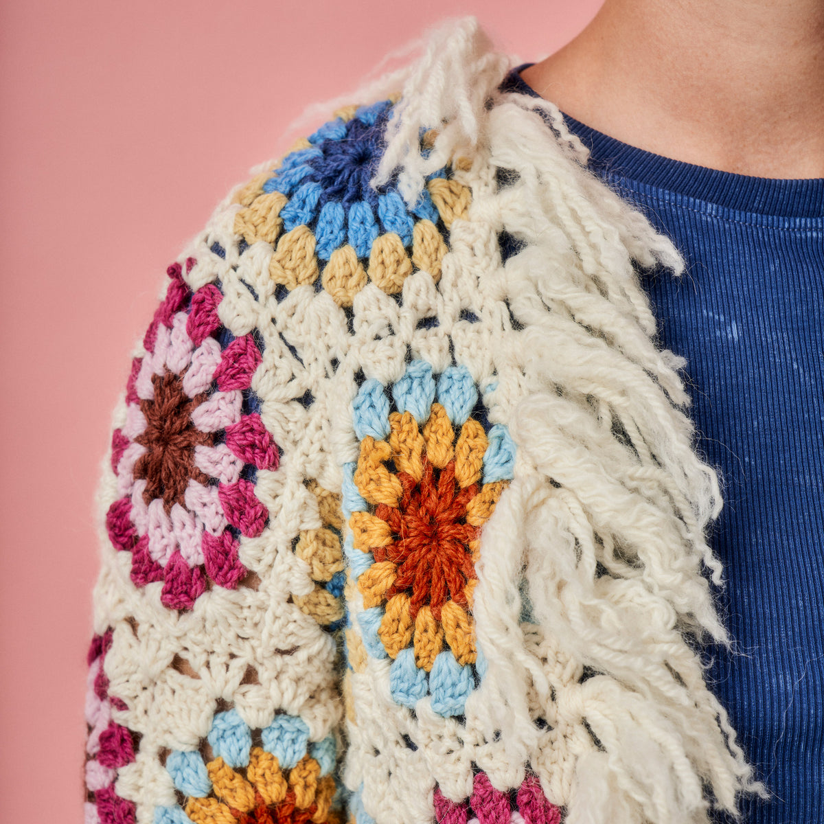 Colorful crocheted shawl with fringe on a pink background