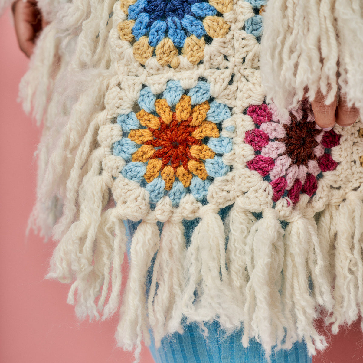 Close-up of a colorful crocheted blanket with tassels on a pink background