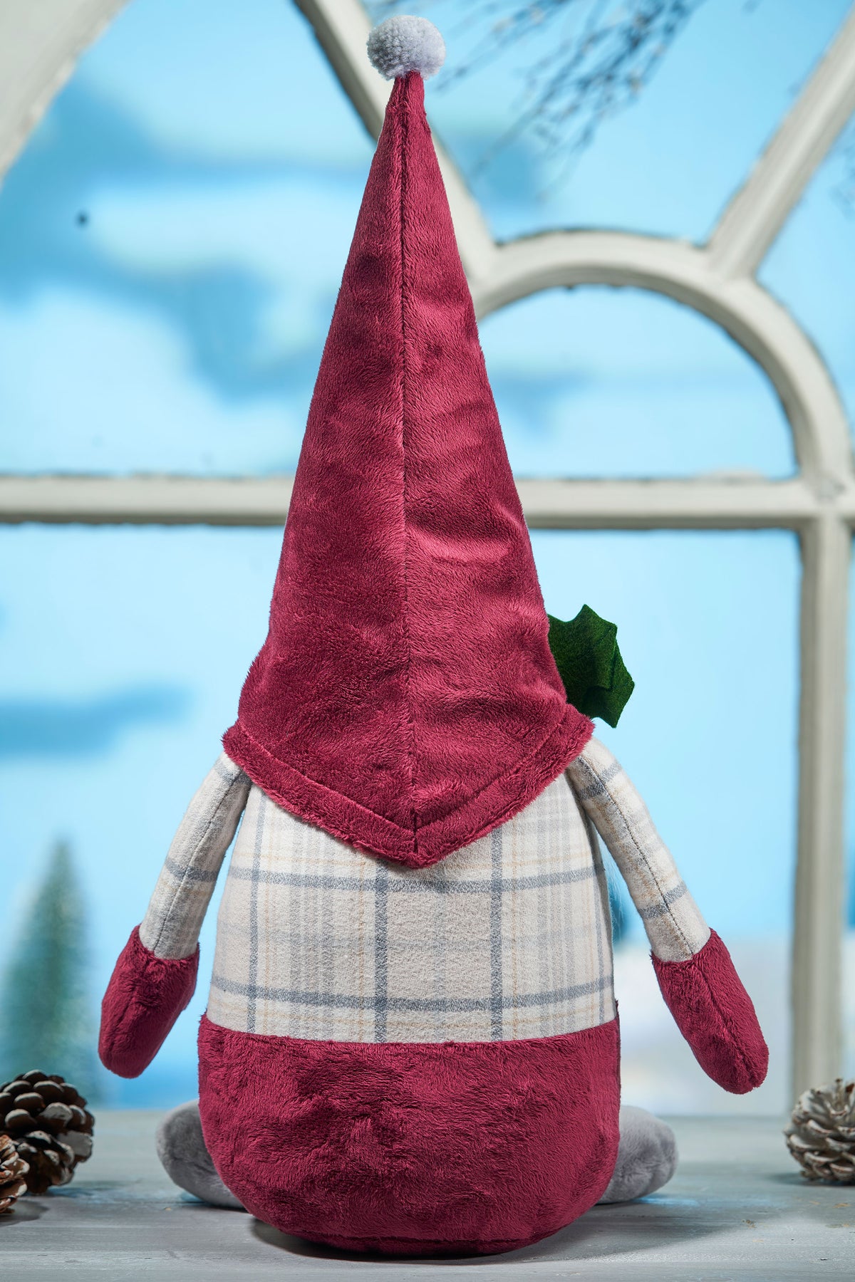 Plush gnome toy with a red hat and plaid outfit on a light blue background