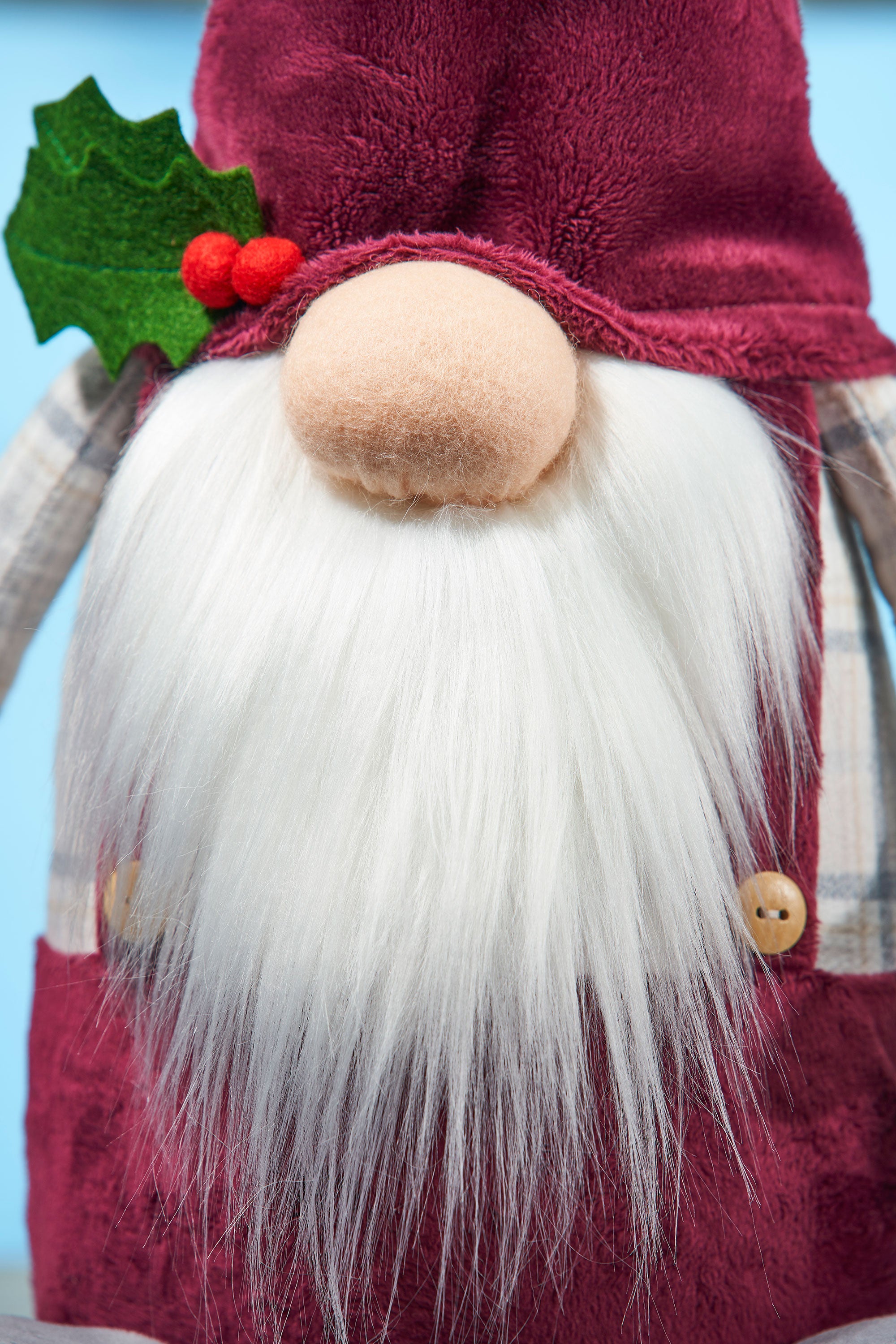 Gnome figure with a beard, red outfit, and holly leaf on a blue background