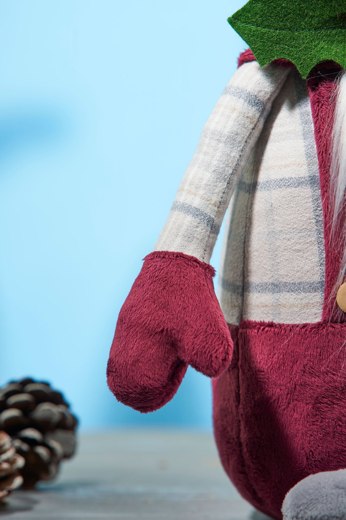 Plush gnome with red mittens and a plaid scarf against a blue background