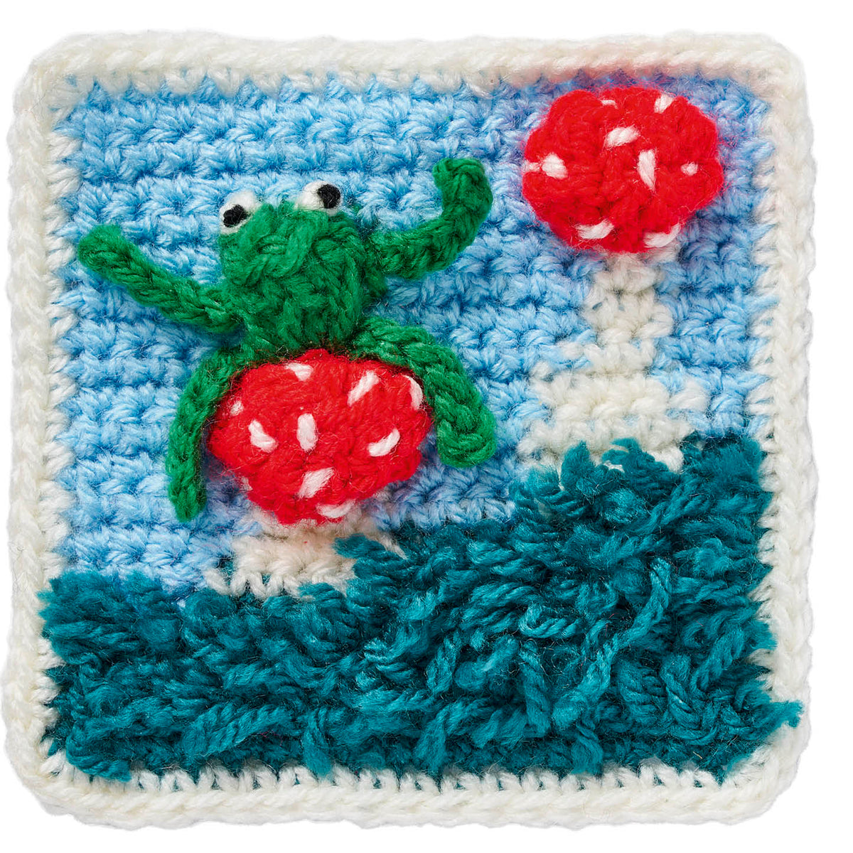 Crocheted square with a green frog and red mushrooms on a blue background