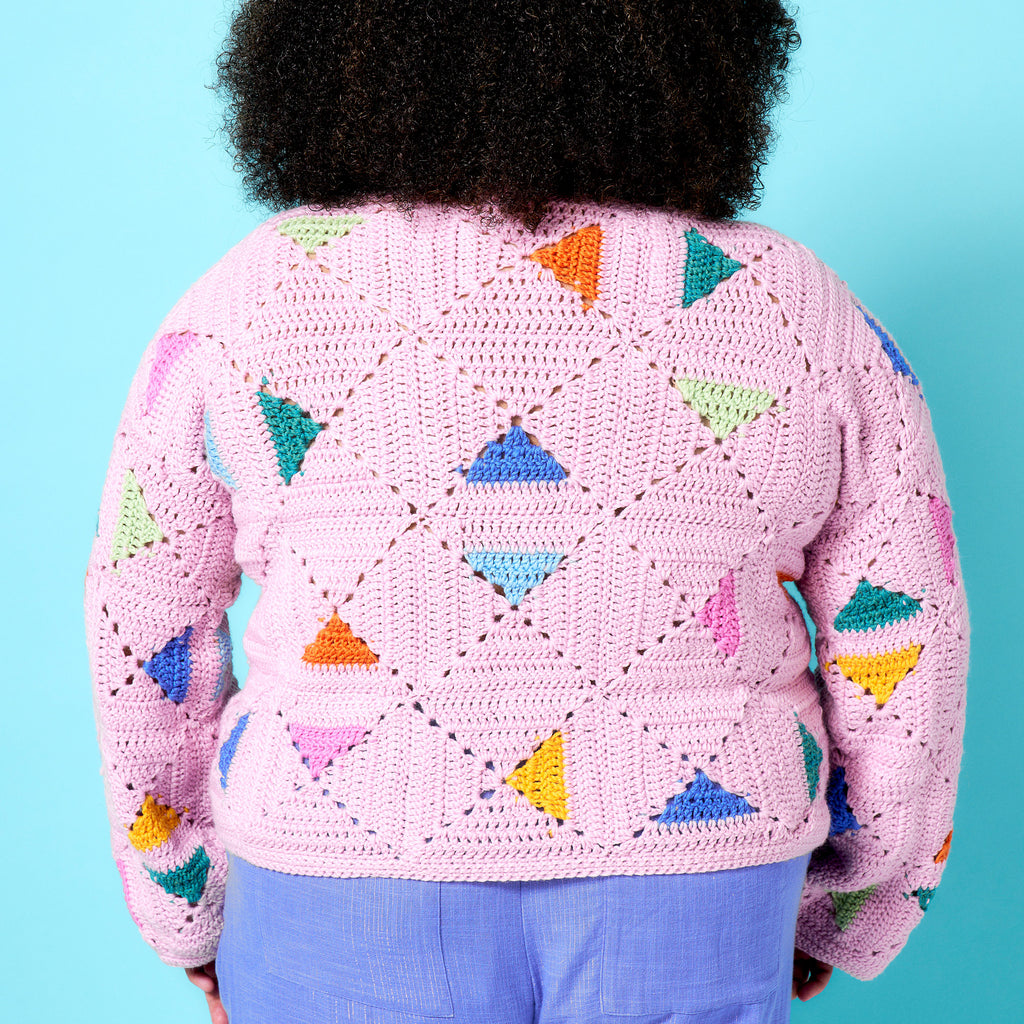Person wearing a pink crochet sweater with colorful triangle patterns against a blue background