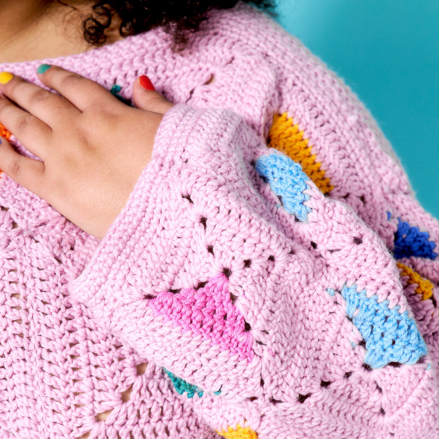 Close-up of a pink knitted garment with colorful patches against a blue background