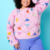 Person wearing a pink crochet sweater with colorful diamond patterns against a blue background