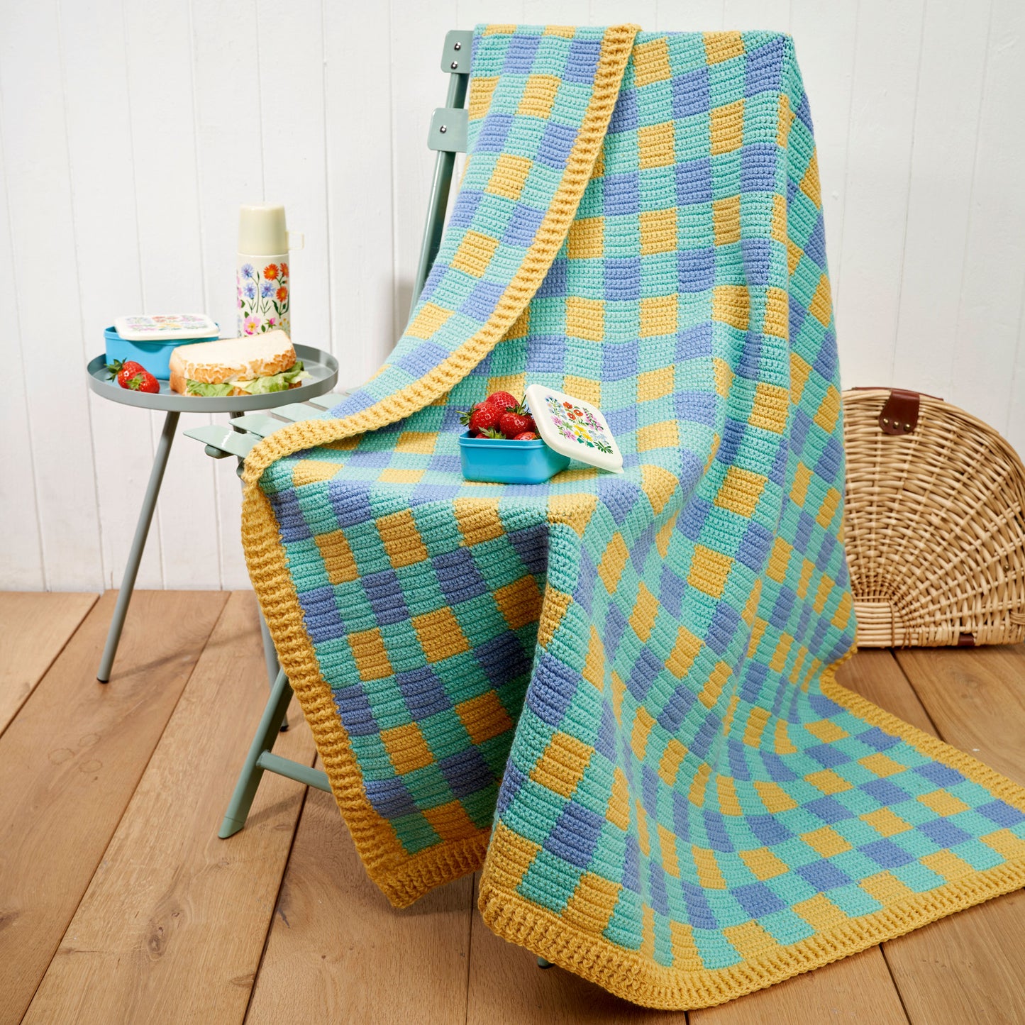 Colorful checkered blanket draped over a chair with a small table and basket in the background.