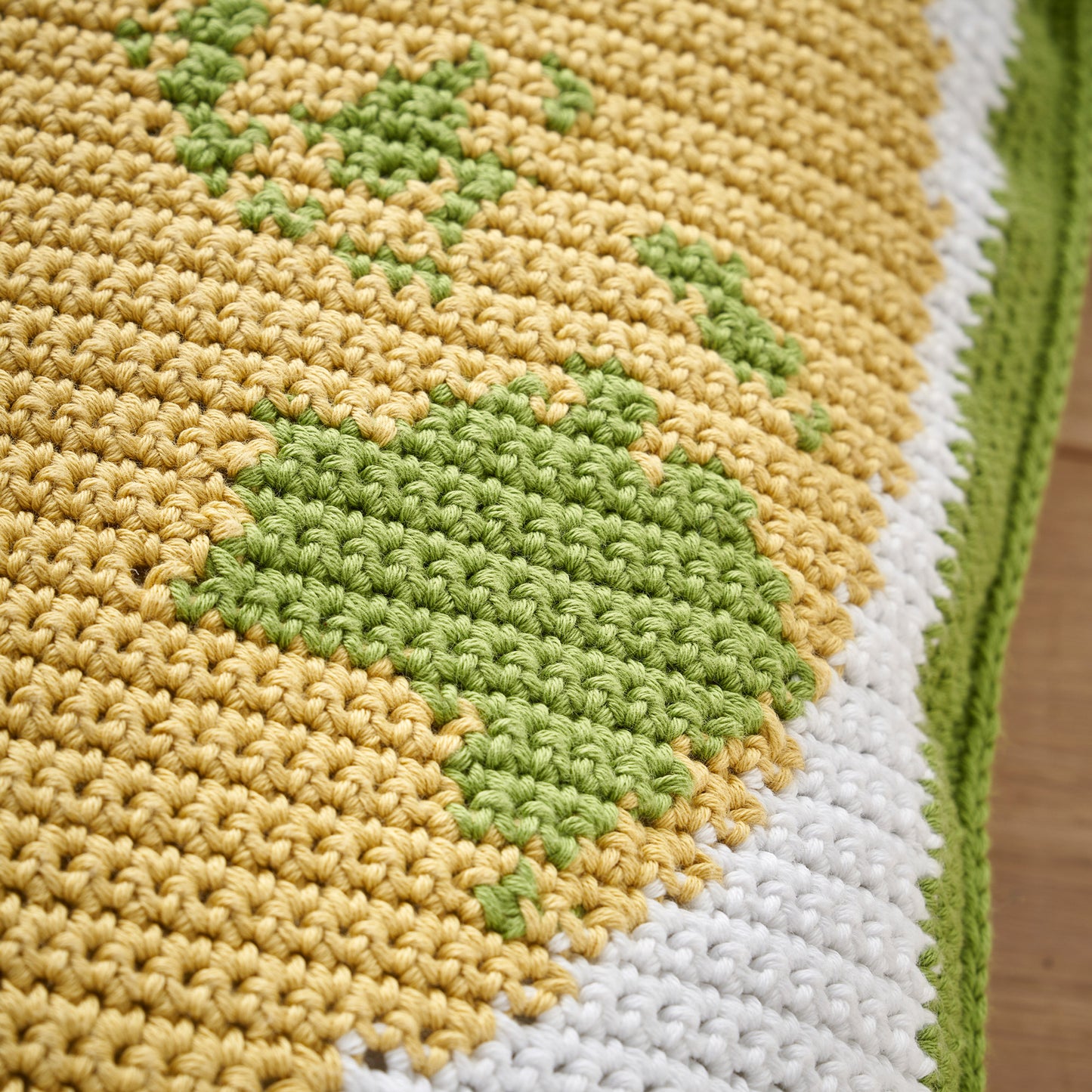 Close-up of a crocheted blanket with green, yellow, and white pattern