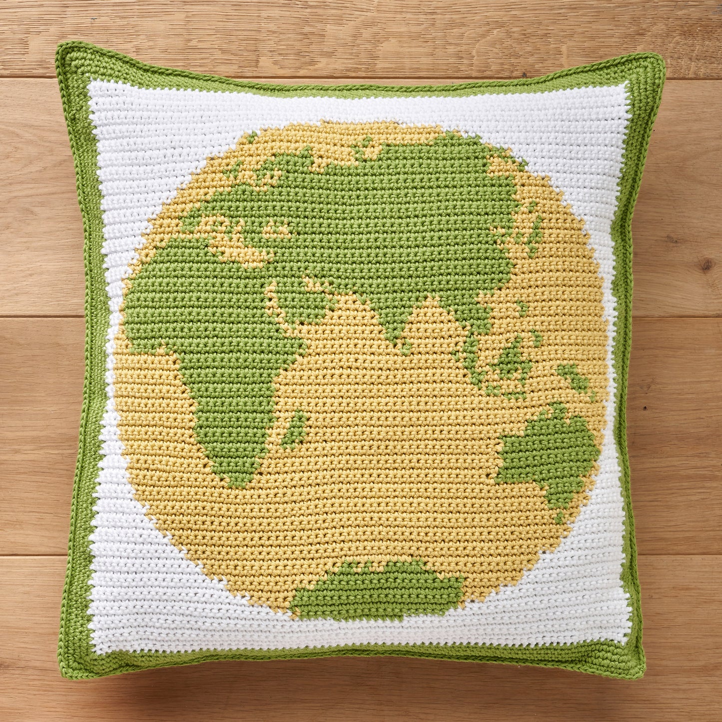 Crocheted pillow with a yellow and green globe design on a wooden surface