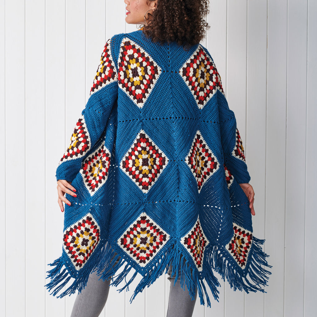 Woman wearing a blue crocheted poncho with geometric patterns against a white background