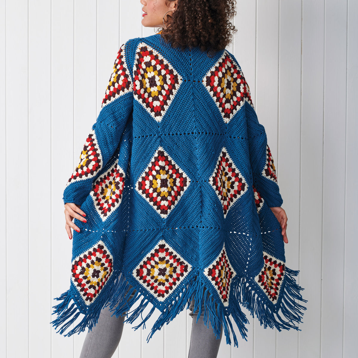 Woman wearing a blue crocheted poncho with geometric patterns against a white background