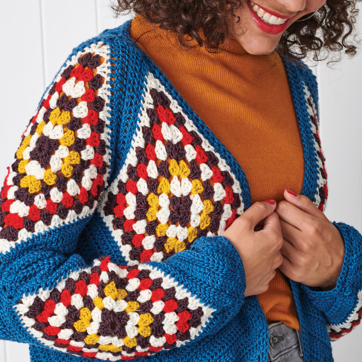 Woman wearing a colorful crochet cardigan over an orange sweater on a white background