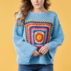 Person wearing a blue crochet sweater with a colorful square pattern on a yellow background