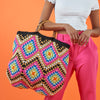 Colorful crocheted bag held by a person against an orange background