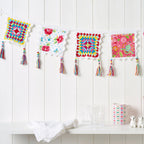 Colorful crochet squares with tassels hanging on a white wall.