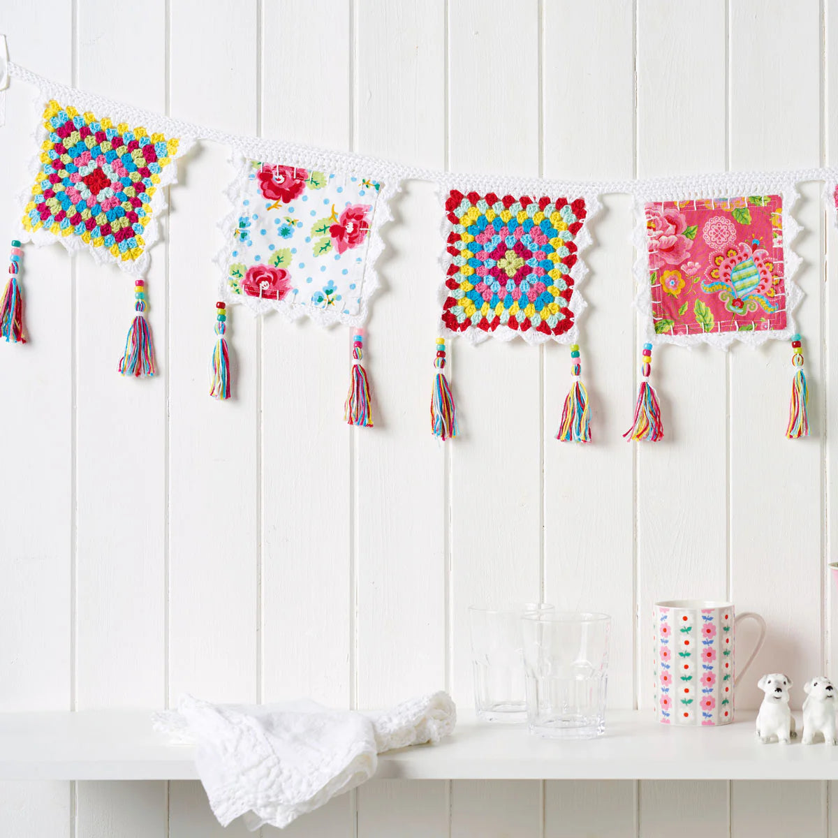 Colorful crochet squares with tassels hanging on a white wall.