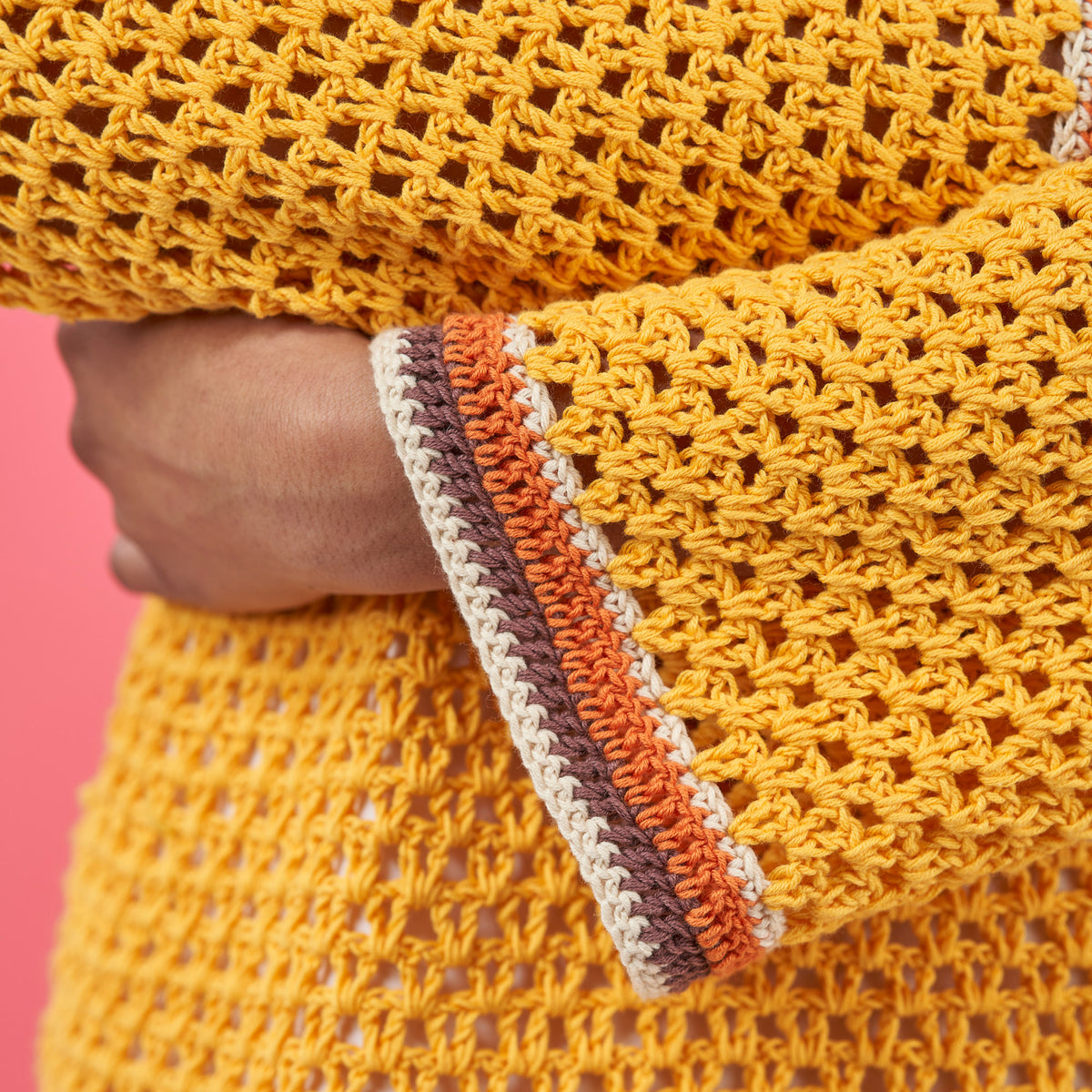 Close-up of a yellow crocheted fabric with a colorful border against a pink background