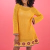 Woman wearing a yellow crochet dress with floral patterns on a pink background