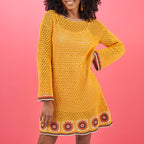 Woman wearing a yellow crochet dress with floral patterns on a pink background