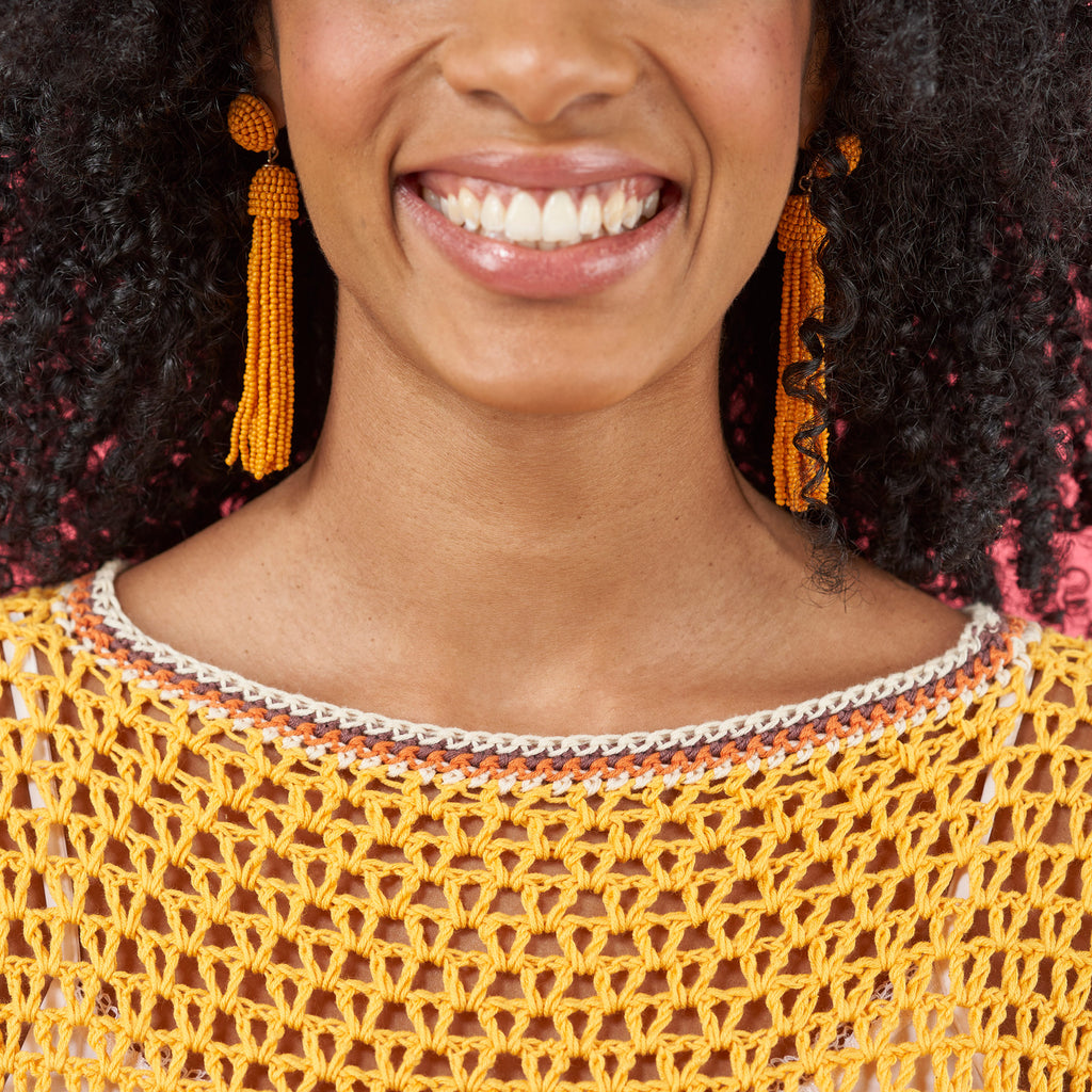 Woman wearing a yellow crochet top and orange tassel earrings with a blurred background