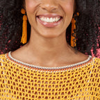 Woman wearing a yellow crochet top and orange tassel earrings with a blurred background