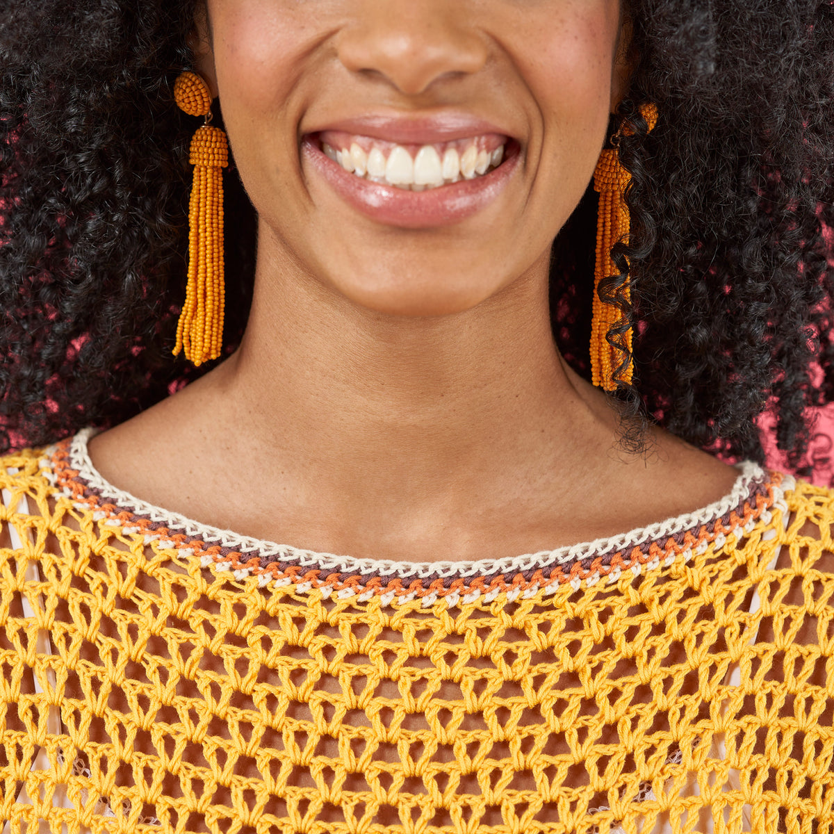 Woman wearing a yellow crochet top and orange tassel earrings with a blurred background