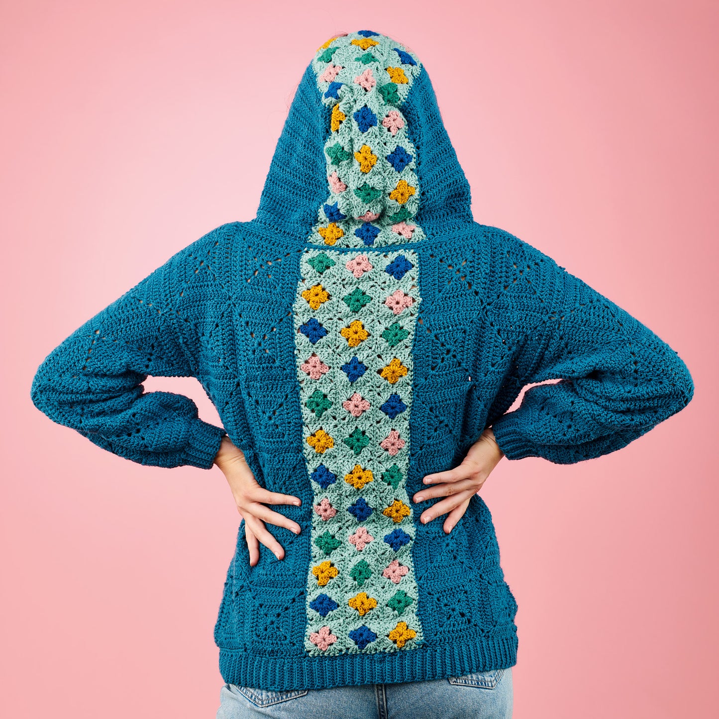 Blue crochet hoodie with a colorful pattern on a pink background