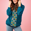 Woman wearing a blue crochet sweater with a colorful pattern on a pink background