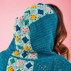 Person wearing a blue crocheted hoodie with floral patterns on a pink background