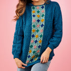 Person wearing a blue crochet cardigan with a colorful pattern on a pink background