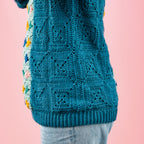 Teal crocheted sweater with colorful accents on a pink background