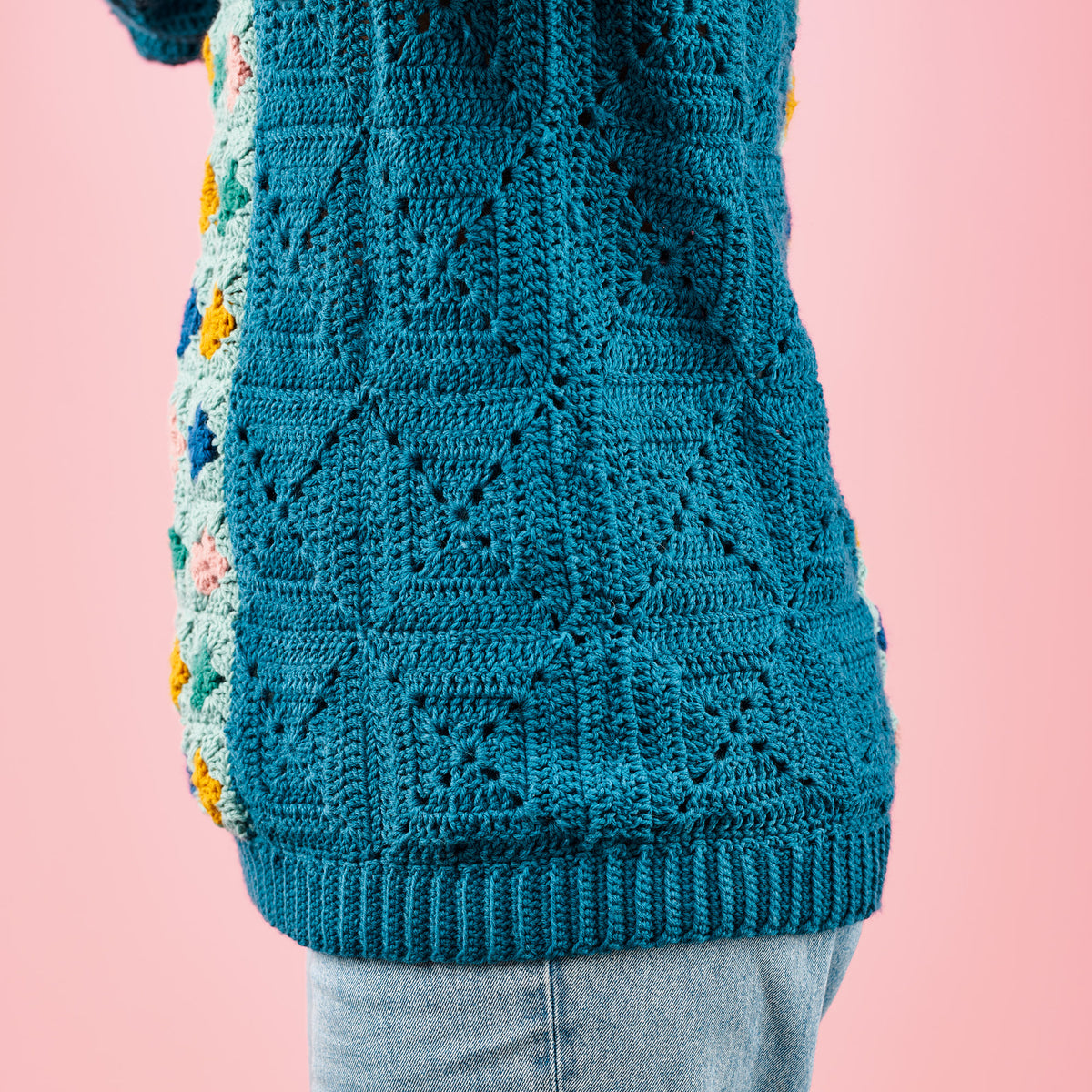 Teal crocheted sweater with colorful accents on a pink background