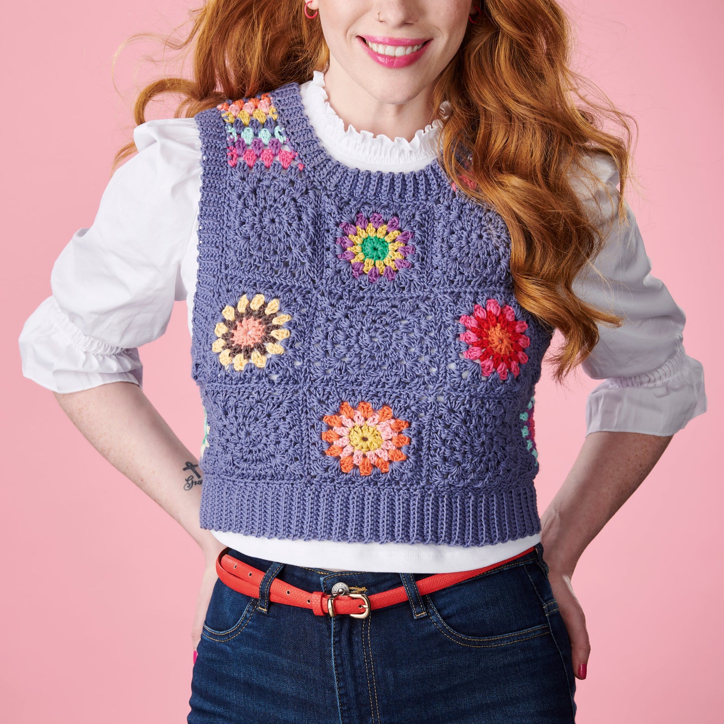 Woman wearing a colorful crochet vest against a pink background