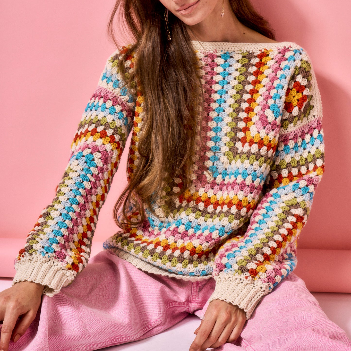 Person wearing a colorful crochet sweater against a pink background
