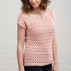 Woman wearing a pink crochet top against a white brick wall.