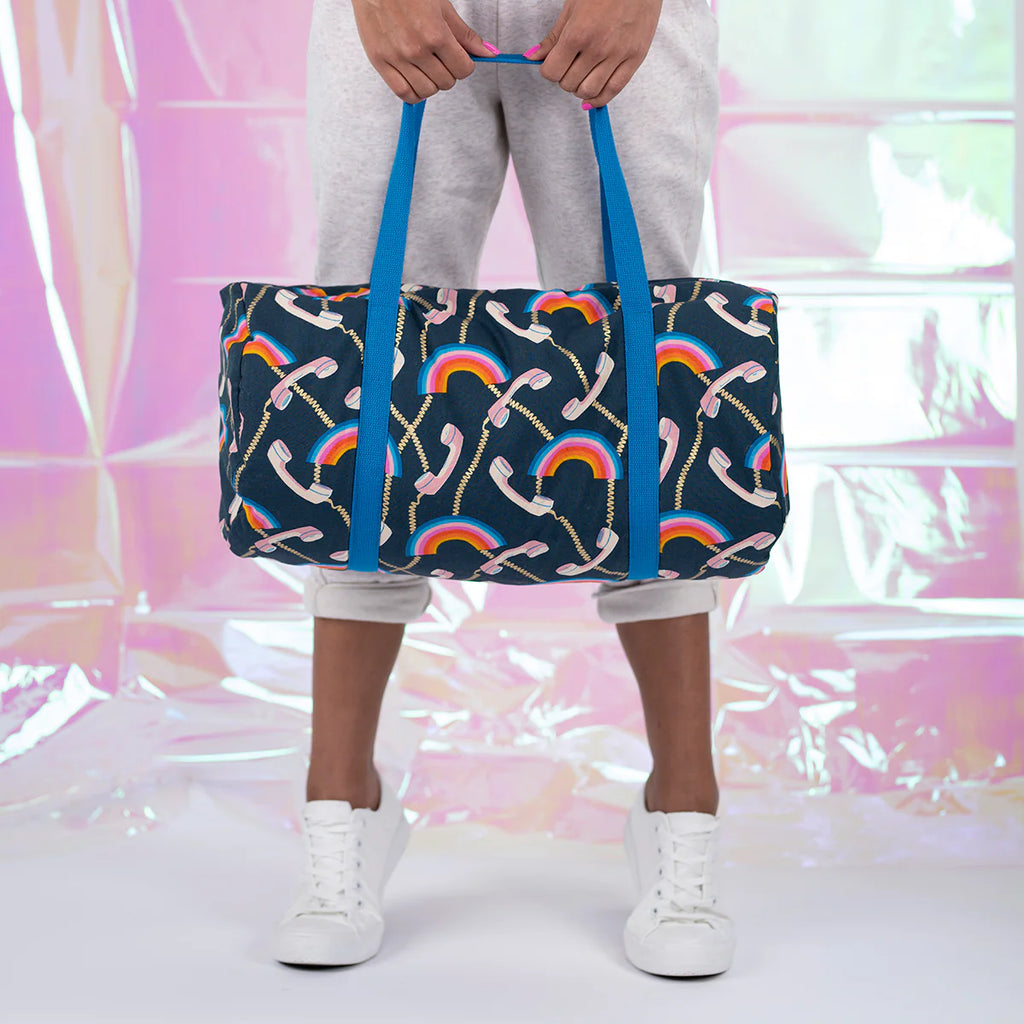 Person holding a navy blue bag with colorful patterns against a pink and white abstract background