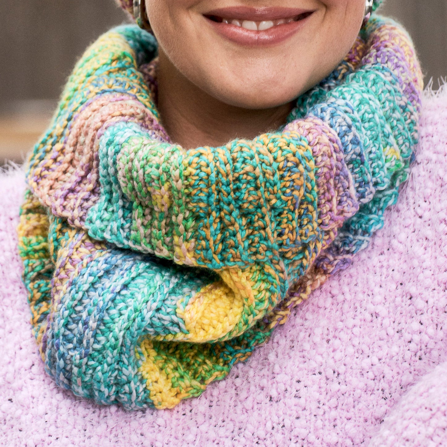 Multicolored crochet scarf worn by a person on a pink blanket