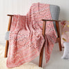 Pink crocheted blanket draped over a wooden chair against a white wall.
