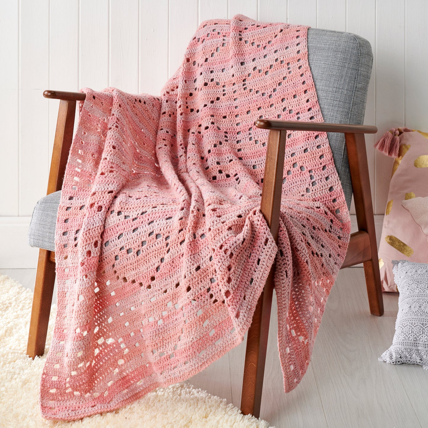 Pink crocheted blanket draped over a wooden chair against a white wall.