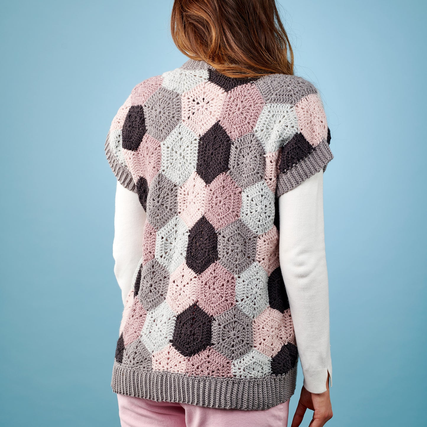 Person wearing a hexagonal patterned crochet vest against a blue background