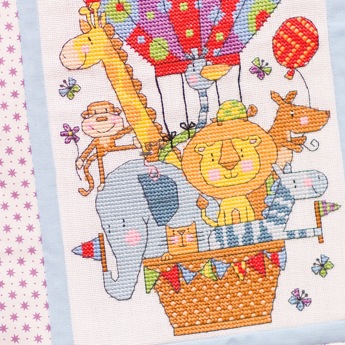 Cross-stitched design of animals in a hot air balloon with colorful balloons and stars.